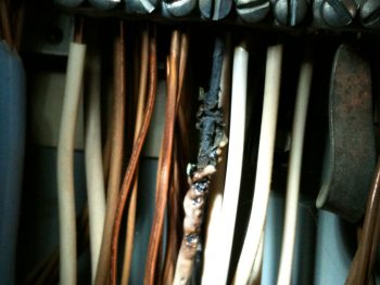 Loose neutral under screw in the electrical panel. Photo of a white wire that has been charred.