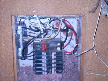 A photo of an electrical panel located in a shop with a rats nest inside of it.